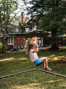 a little girl sitting on a swing in a yard at Chalet Alpin Walk to Lake and Beach with Spa and BBQ in Huberdeau