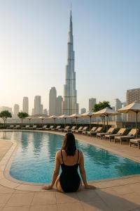 a woman in a black dress sitting next to a swimming pool at Vida Dubai Mall! 2 Bedroom with Burj Khalifa View! Direct Access to Dubai Mall in Dubai