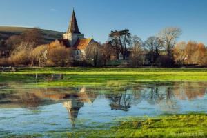 le reflet d'une église dans un champ avec un étang dans l'établissement Alfriston Lodge By Air Premier, à Alfriston