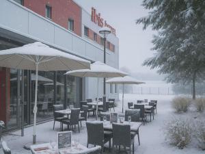 a restaurant with tables and umbrellas in the snow at Ibis Saint-Genis-Pouilly Genève in Saint-Genis-Pouilly