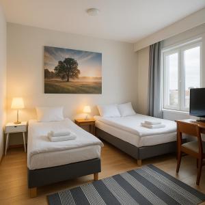 a room with two beds and a desk and a television at Hotelli Vilho in Kotka