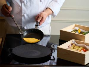 a man cooking food in a pan on a stove at Nagoya Kanko Hotel in Nagoya