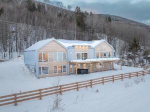 a wooden house in the snow with a fence at Phil Good 1219: Luxurious River View in Charlevoix in Petite-Rivière-Saint-François