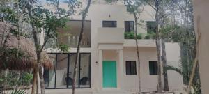 un bâtiment blanc avec une porte verte et des arbres dans l'établissement Casabel Tulum jungle experience, à Cobá