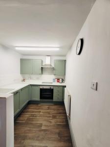 a kitchen with green cabinets and a clock on the wall at Above the Bear in Wiveliscombe