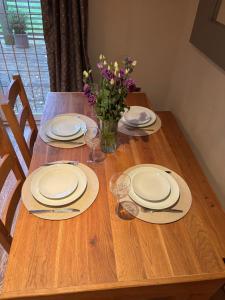 une table en bois avec des assiettes et des verres et un vase de fleurs dans l'établissement Surrounded by fields just 3 miles from Stratford - upon Avon - Alveston Pastures Retreat, à Stratford-upon-Avon 9 autres photos