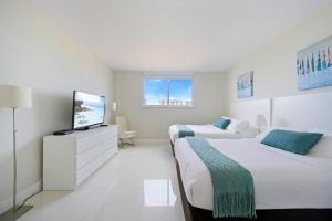 a white bedroom with two beds and a tv at Ocean Reserve 1524 in Miami Beach +35 photos