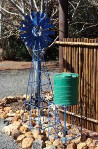 a blue windmill and a green bucket next to a fence at Blou Windpomp Guest Lodge in Delmas