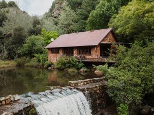 a log cabin next to a waterfall next to a river at Migrate Portfolio in Dullstroom