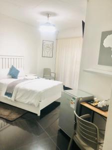 Schlafzimmer mit einem weißen Bett, einem Schreibtisch und einem Stuhl in der Unterkunft 2 Seasons Guesthouse East London in East London