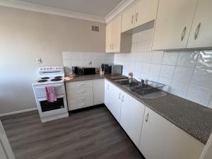 グラフトンにあるApartments on Turf Unit 4のキッチン(白いキャビネット、コンロ、シンク付)