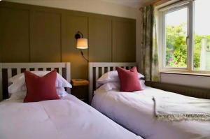 two beds with red pillows in a room with a window at Nikolaus Cottage Cotswolds in Winchcombe