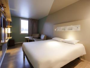 een hotelkamer met een groot wit bed en een stoel bij ibis budget Albertville in Gilly-sur-Isère