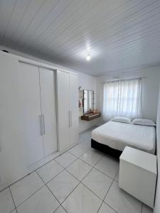 a white bedroom with a bed and a window at Apartamento Orquídea in Porto Belo