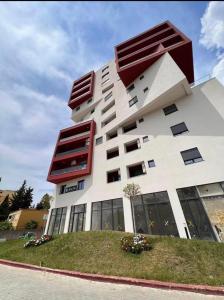 a large white building with red windows and grass at Class Apartments in Tirana