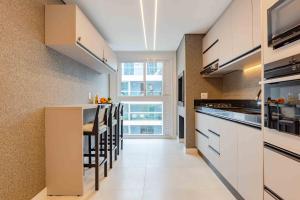 a kitchen with white cabinets and a bar with stools at Apartamento Lindíssimo na Praia de Bombas in Bombas
