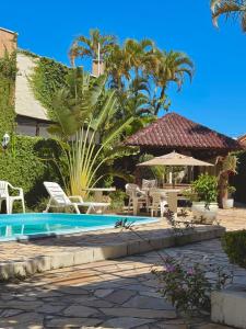 a pool with chairs and an umbrella and palm trees at Pousada Volare in Matinhos