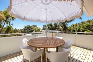 a wooden table and chairs on a balcony with an umbrella at Bay Haven - Walk to Palm Beach in Waiheke Island