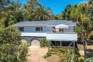a white house with a balcony and palm trees at Bay Haven - Walk to Palm Beach in Waiheke Island
