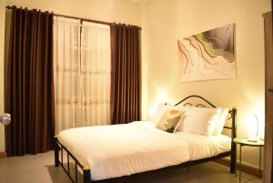 a bedroom with a bed with white sheets and a window at Khwanlom House in Lampang