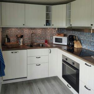 une cuisine avec des armoires blanches, un évier et un micro-ondes dans l'établissement Newly Renovated Cottage With Sea View In Säckebäck, à Varekil