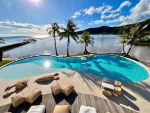 a swimming pool with lounge chairs and a body of water at APATOA Beach & Garden Village in Raiatea