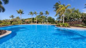 a large swimming pool with palm trees in the background at SUMMER BREEZE Sunny 2BR Kulalani Home Next To Community Pool in Waikoloa