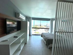 une chambre avec un lit et une télévision et un balcon dans l'établissement Eu Amo Arraial Hospedagem - Studio Sophia I Vista Mar, à Arraial do Cabo