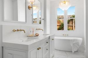 a white bathroom with a tub and a sink and mirror at Farmhouse Hunter Valley in Pokolbin