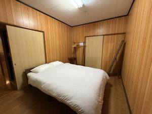Un dormitorio con una cama blanca con paredes de madera. en 館山市犬石戸建 自然に囲まれた森のコテージ 6DK 最大18名宿泊可 パーティー BBQ 花火ok, en Tateyama