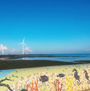 uma vista para uma praia com um moinho de vento ao fundo em Bae Bae Guesthouse em Jeju