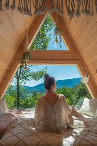 a woman sitting on a bed looking out of a window at Alemiło mini - domek z balią i widokiem na Babią Górę in Zawoja