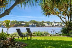 two chairs sitting on the grass near the water at Family Beach House at Twin Waters Resort in Twin Waters
