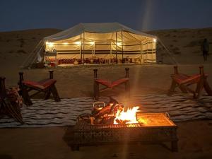 a fire pit in the sand with a tent in the background at Sand Oasis camp in Ḩawīyah