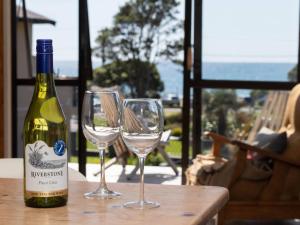 a bottle of wine and two wine glasses on a table at Aqua Vista On Arden - beachfront bach in Oakura in Oakura