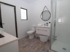 a white bathroom with a toilet and a mirror at Aqua Vista On Arden - beachfront bach in Oakura in Oakura +13 photos