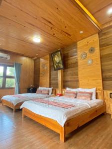 two beds in a room with wooden walls at Lá Homestay in Ðak Lao