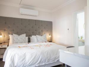 een witte slaapkamer met een groot wit bed met bloemen erop bij La Dolce Vita Gordon’s Bay in Gordonsbaai