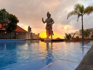 une statue à côté d'une piscine avec un coucher de soleil en arrière-plan dans l'établissement Pooja Ocean View Cottage, à Nusa Penida