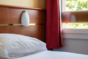 een bed met een wit kussen en een raam bij Brit Hotel Agen - L'Aquitaine in Le Passage +39 foto's