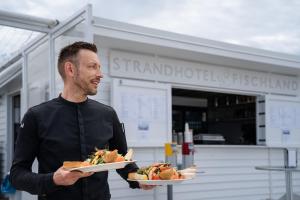a man is holding two plates of food at Strandhotel Fischland in Dierhagen +95 photos