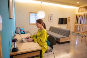 ein junges Mädchen sitzt an einem Tisch mit einem Laptop in der Unterkunft Ittokasi Ao no Ie - Vacation STAY 44156v in Fuefuki
