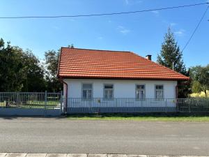 a white house with an orange roof and a fence at Gólyafészek Vendégház in Szécsény