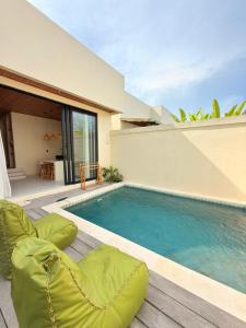 a swimming pool with green chairs next to a house at Villa Saraswati I in Uluwatu