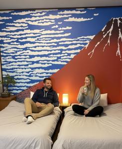 Zwei Personen sitzen auf Betten in einem Zimmer mit einem Bergmotiv. in der Unterkunft ミラージュ宿 2025年5月オープン 京都芸術 1軒家貸切 in Kyoto