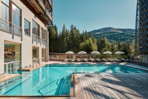 a swimming pool with chairs and a building at Falkensteiner Aktiv & Familienhotel Cristallo Superior in Katschberghöhe +27 photos