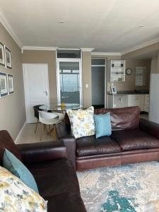 a living room with a brown leather couch and a table at Oceana Views in Gordonʼs Bay