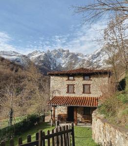 ein Steinhaus mit einem Zaun und Bergen im Hintergrund in der Unterkunft Casa La Ribera in Lon
