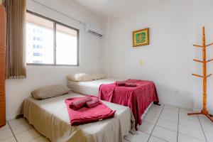a room with two beds with pink sheets and a window at Apartamento com Varanda, Churrasqueira e Vista Mar in Meia Praia