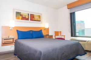a bedroom with a bed with blue pillows and a window at Hotel Galerías Express in Tepatitlán de Morelos